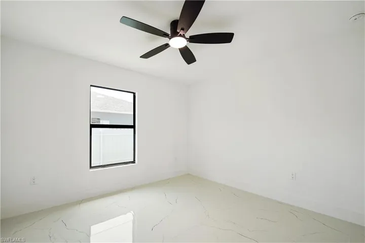 This space features a contemporary ceiling fan with a light fixture, a window providing natural light, and light-colored flooring with a subtle pattern