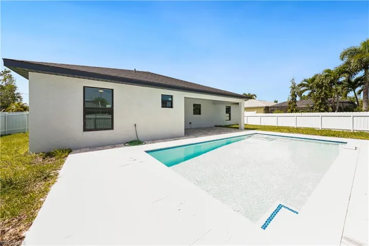 The property features a private swimming pool with a white tiled deck, a covered patio, and a white fence enclosing the yard