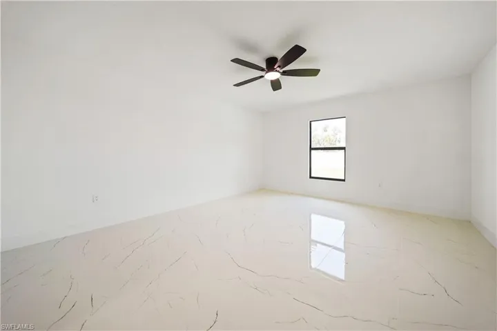 This room features bright white walls, a single window with a dark frame, and a ceiling fan with dark blades