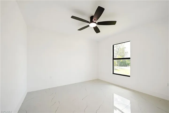 This room features a ceiling fan with integrated lighting, a window with dark framing, and light-colored tiled flooring