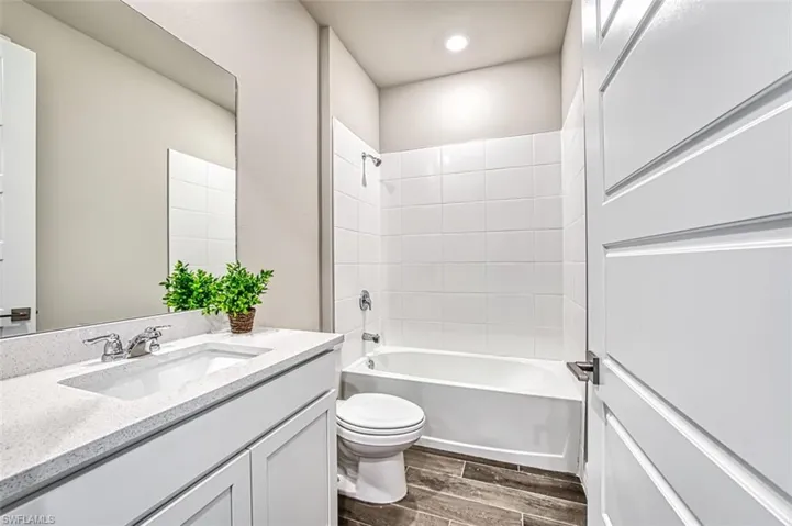 Full bathroom featuring tiled shower / bath combo, vanity with extensive cabinet space, toilet, and hardwood / wood-style floors