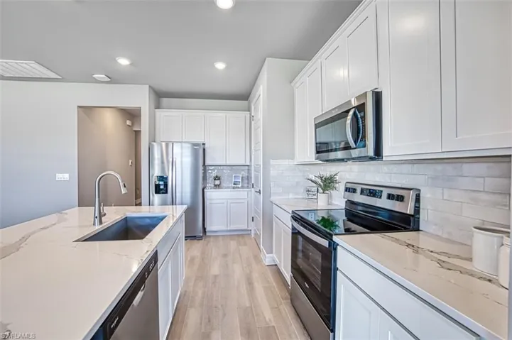 Kitchen featuring light wood-type flooring, appliances with stainless steel finishes, white cabinets, sink, and tasteful backsplash