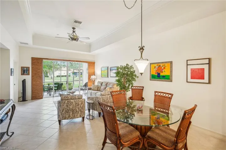 Tiled dining space with ceiling fan, a raised ceiling, and ornamental molding