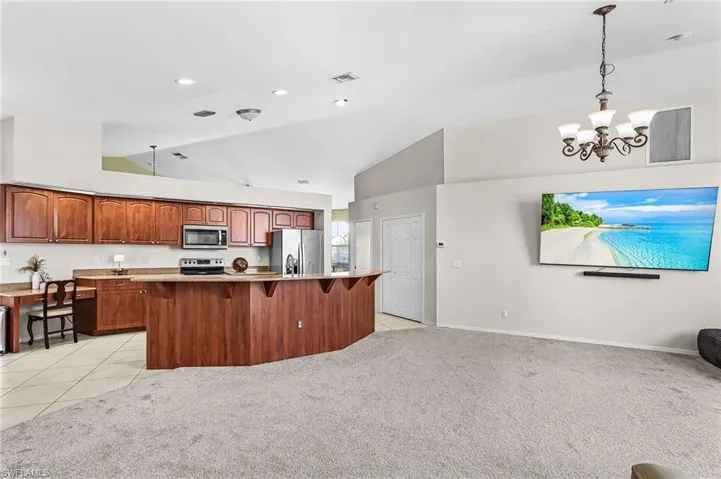 Kitchen with a kitchen breakfast bar, light colored carpet, stainless steel appliances, lofted ceiling, and a kitchen island