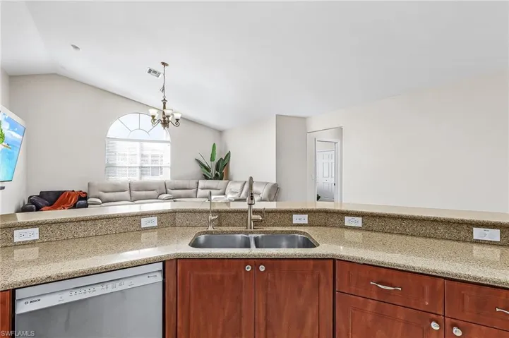 Kitchen featuring open floor plan, light stone countertops, dishwasher, suspended lighting, and vaulted ceiling