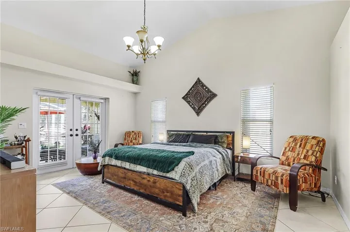 Bedroom featuring access to exterior, french doors, vaulted ceiling, light tile patterned floors, and a chandelier
