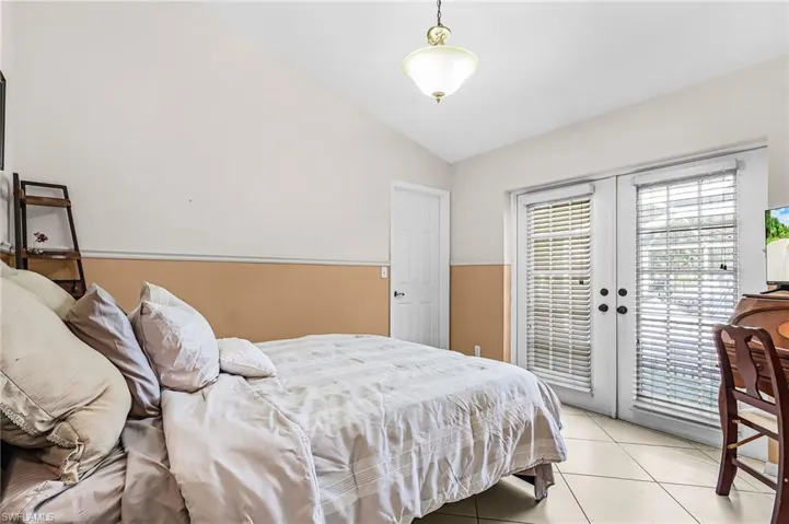 Bedroom featuring vaulted ceiling, access to exterior, light tile patterned floors, and french doors