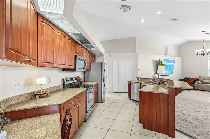 Kitchen with stainless steel appliances, a breakfast bar area, vaulted ceiling, a kitchen island with sink, and light stone countertops