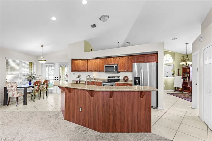 Kitchen featuring a breakfast bar area, vaulted ceiling, stainless steel appliances, light stone counters, and light tile patterned floors