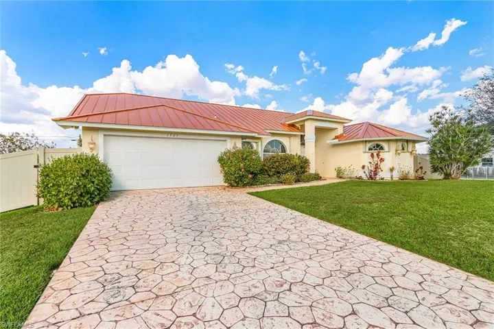 View of front of property featuring stucco siding, a garage, driveway, and a metal roof