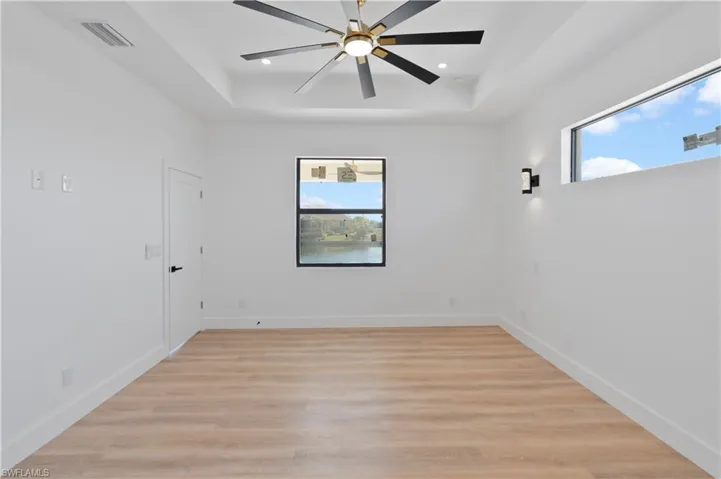 Empty room with light wood-type flooring, a tray ceiling, and ceiling fan