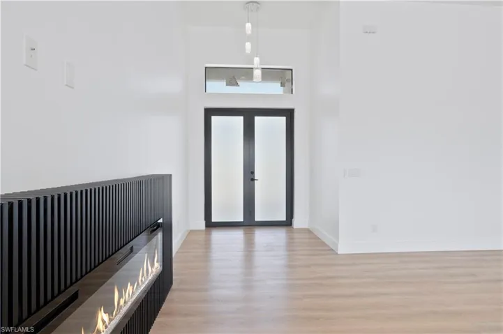 Foyer with light wood-style flooring, a high ceiling, french doors, and a glass covered fireplace