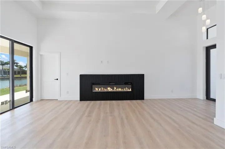 Unfurnished living room with a high ceiling, a glass covered fireplace, light wood-style floors, and a water view
