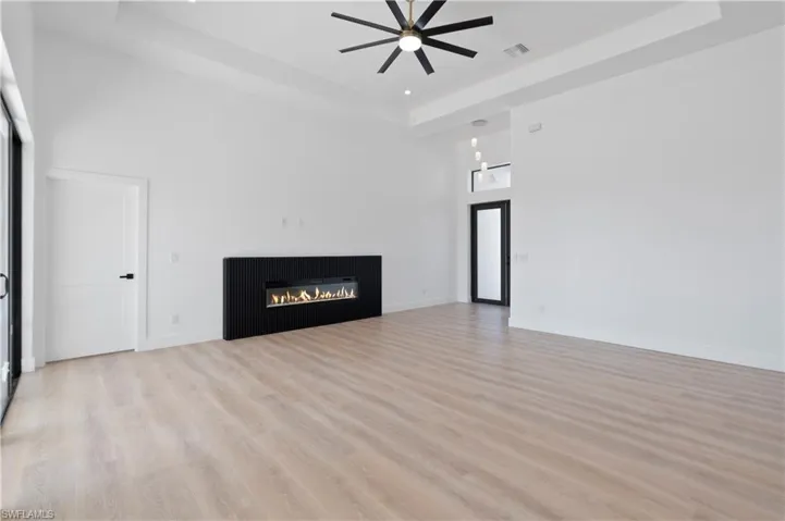 Unfurnished living room with light wood-style floors, a raised ceiling, a glass covered fireplace, a ceiling fan, and recessed lighting