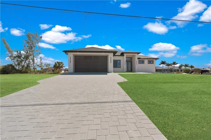 Prairie-style house featuring a front lawn, decorative driveway, an attached garage, and stucco siding