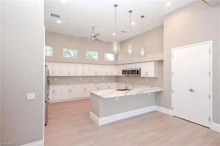 Social Room Kitchen featuring a towering ceiling, white cabinets, hanging light fixtures, a kitchen breakfast bar, and a peninsula