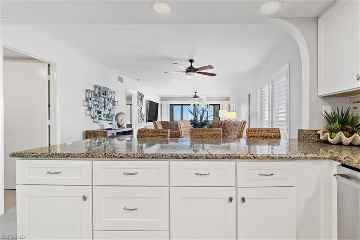 Kitchen with ceiling fan, white cabinetry, kitchen peninsula, and stone counters