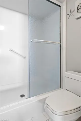 Bathroom with tile patterned floors, toilet, and a shower with door
