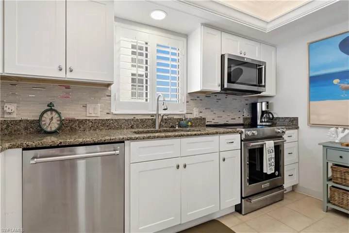 Kitchen featuring decorative backsplash, appliances with stainless steel finishes, dark stone counters, sink, and white cabinets