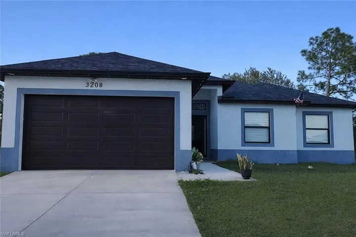 View of front facade featuring a front lawn, a shingled roof, driveway, stucco siding, and an attached garage