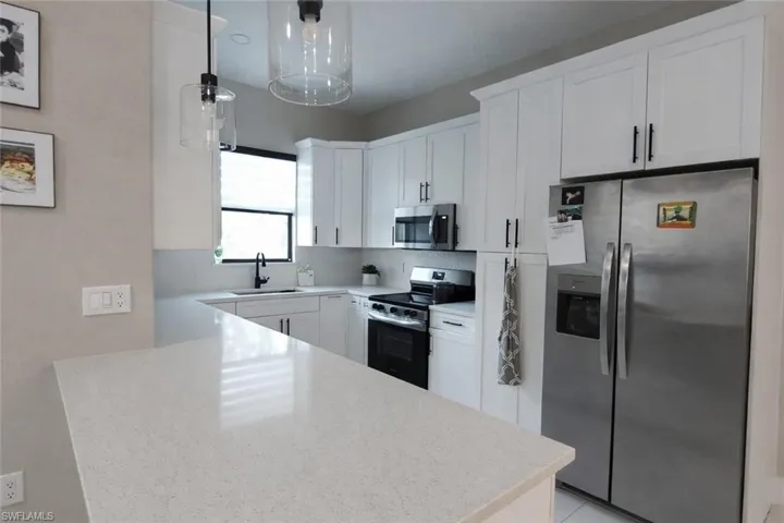 Kitchen featuring stainless steel appliances, white cabinetry, light stone counters, decorative light fixtures, and a peninsula