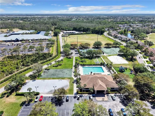 Expansive community recreation area featuring a large swimming pool, multiple tennis courts, a sand volleyball court, and a central clubhouse with a parking area