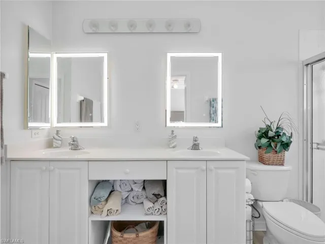 Dual vanity featuring white cabinetry, integrated sinks, chrome faucets, and illuminated mirrors
