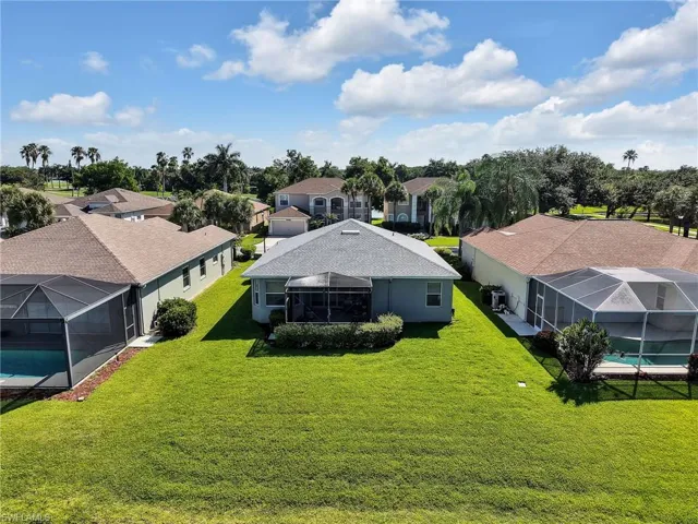 Rear exterior featuring a screened-in lanai, expansive green lawn, and mature landscaping