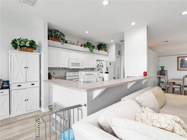 White kitchen cabinetry with a mosaic tile backsplash, light-toned countertops, and recessed lighting
