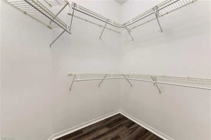 Walk-in closet featuring white wire shelving, hanging rods, white baseboards, and wood-finish flooring