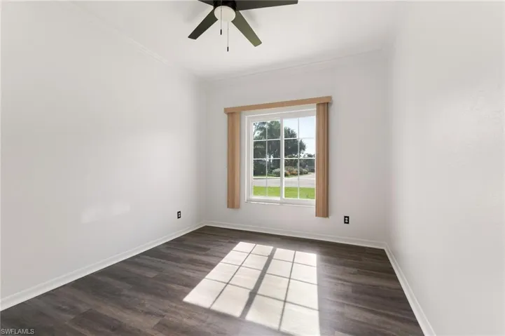Bright room featuring a large window with exterior views, dark wood-finish flooring, white walls, and a ceiling fan