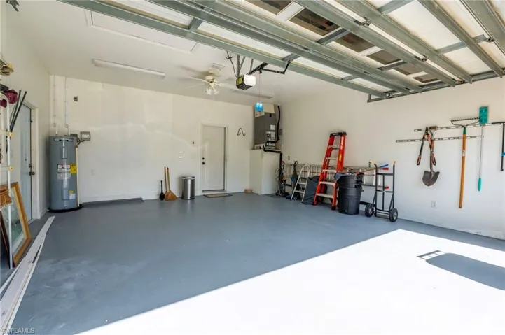Spacious garage featuring a durable floor coating, fluorescent lighting, a ceiling fan, and accessible utility connections