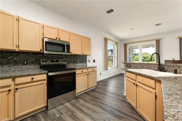 Kitchen featuring wood-finish cabinetry, granite countertops, a mosaic tile backsplash, and stainless steel appliances