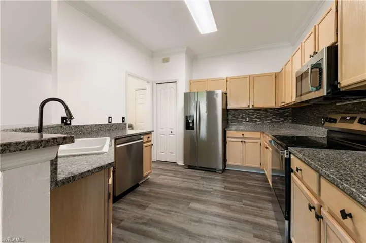 Kitchen featuring wood-finish flooring, granite countertops, light wood cabinetry, a mosaic tile backsplash, and stainless steel appliances