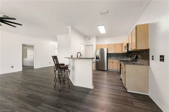 Open-concept kitchen featuring light-toned cabinetry, a mosaic tile backsplash, and dark granite countertops