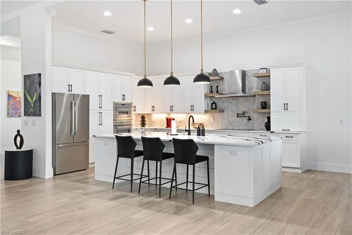 Kitchen with open shelves, ornamental molding, decorative light fixtures, a kitchen island with sink, and light wood-style floors