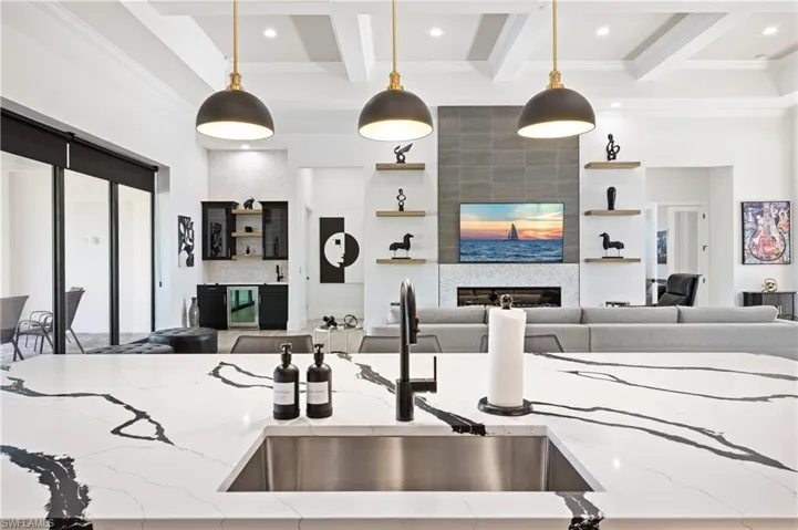 Kitchen with open floor plan, light stone counters, decorative light fixtures, ornamental molding, and wine cooler