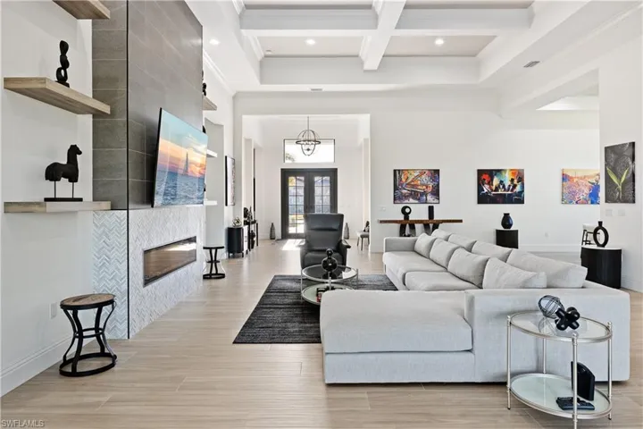 Living room featuring crown molding, coffered ceiling, french doors, light wood finished floors, and a fireplace