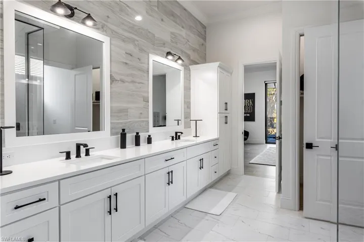 Bathroom featuring double vanity, light marble finish flooring, crown molding, and tile walls