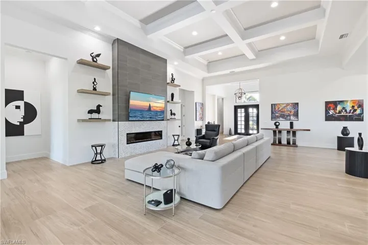 Living room featuring coffered ceiling, a fireplace, light wood finished floors, a chandelier, and french doors