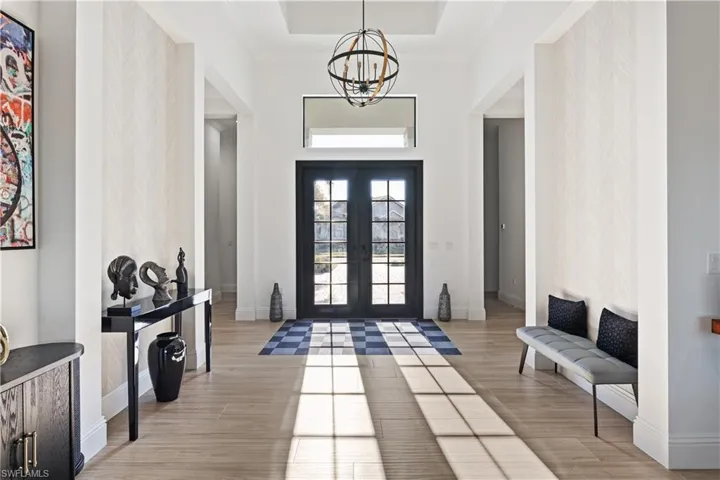 Foyer entrance featuring a chandelier, light wood finished floors, a high ceiling, french doors, and crown molding
