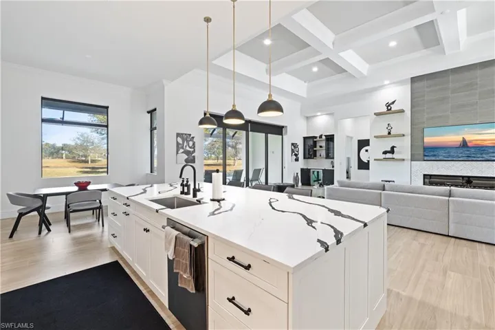 Kitchen featuring white cabinets, hanging light fixtures, light stone counters, light wood finished floors, and a center island with sink