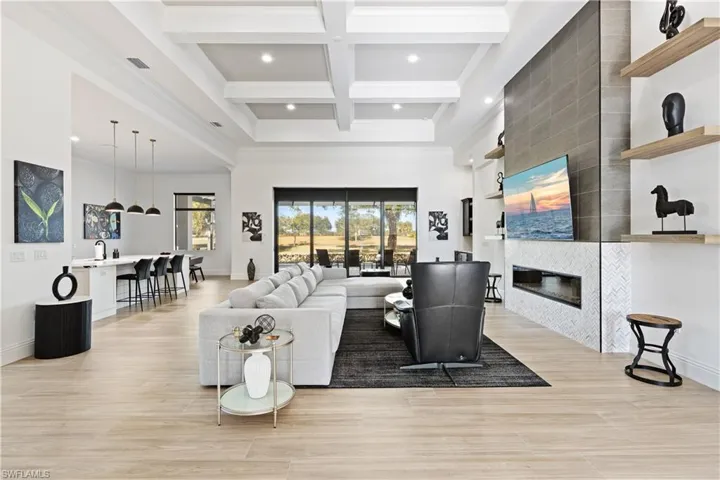 Living room with coffered ceiling, a tiled fireplace, light wood-type flooring, ornamental molding, and recessed lighting