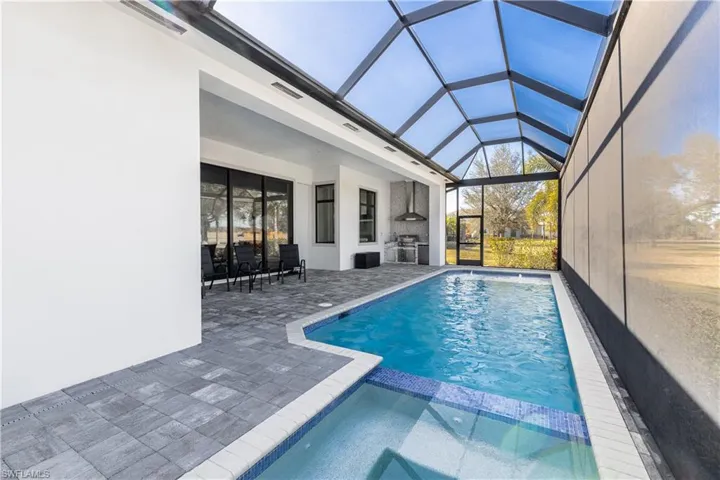 Relaxing pool / spa featuring a sunroom, a patio area, a lanai, and exterior kitchen