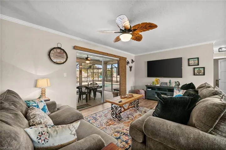 Living room with ornamental molding, wood finished floors, a sunroom, and ceiling fan