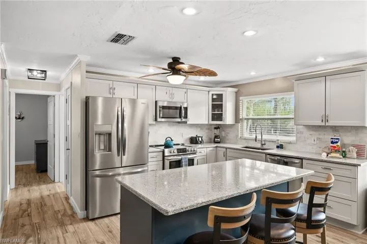 Kitchen with ornamental molding, stainless steel appliances, light stone countertops, a kitchen bar, and glass insert cabinets