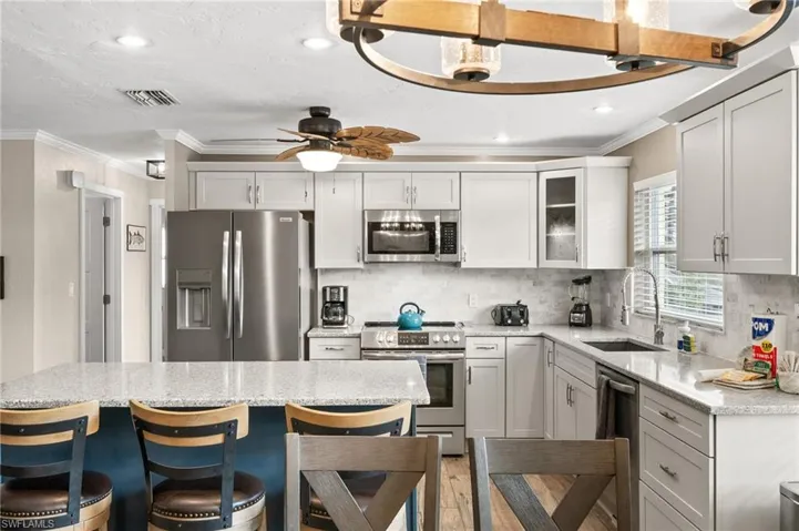 Kitchen featuring appliances with stainless steel finishes, a kitchen bar, light stone counters, glass insert cabinets, and crown molding