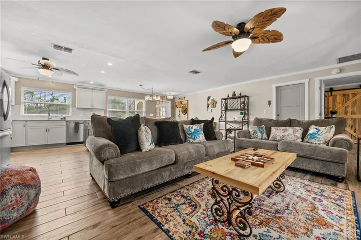 Living room with a ceiling fan, ornamental molding, light wood finished floors, a chandelier, and a barn door