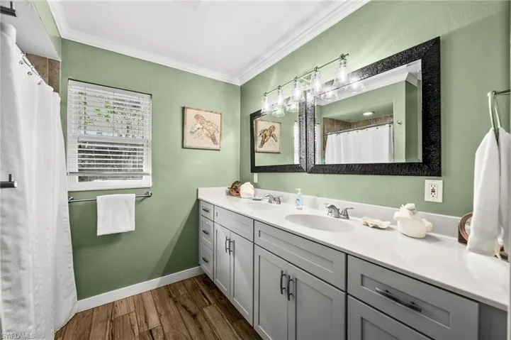 Bathroom with double vanity, dark wood-style flooring, ornamental molding, and a shower with curtain
