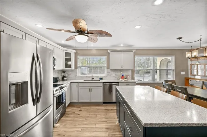 Kitchen featuring stainless steel appliances, light stone countertops, recessed lighting, white cabinets, and a kitchen island